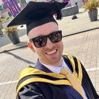 Chris smiling in his graduation cap and gown at Warwick Business School